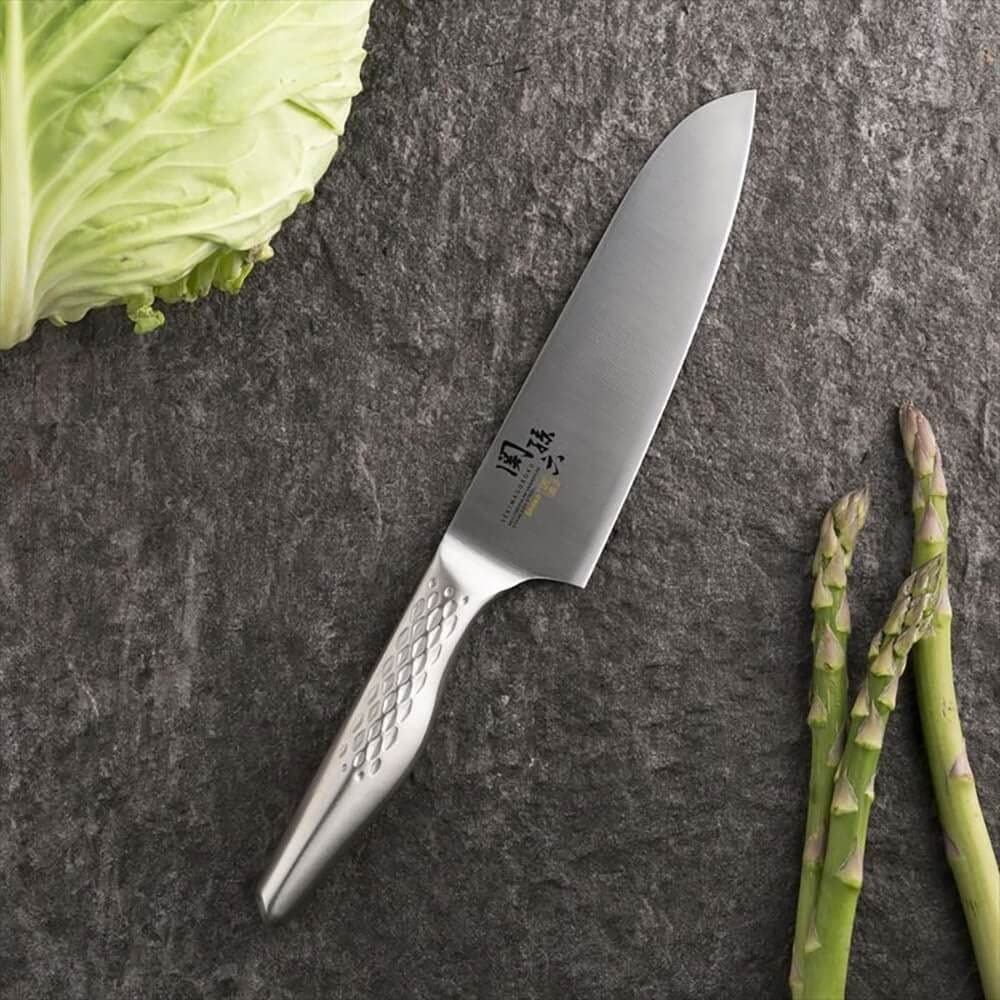Ein Küchenmesser liegt neben Kohl und Spargel auf dunklem Stein.
