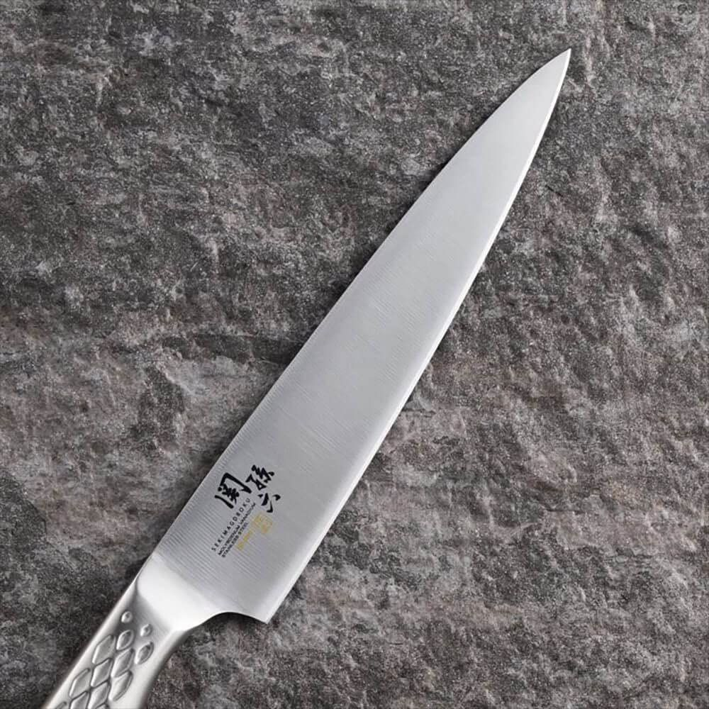 Ein scharfes Küchenmesser mit silberner Klinge und gemustertem Griff liegt auf einem grauen Steinuntergrund.