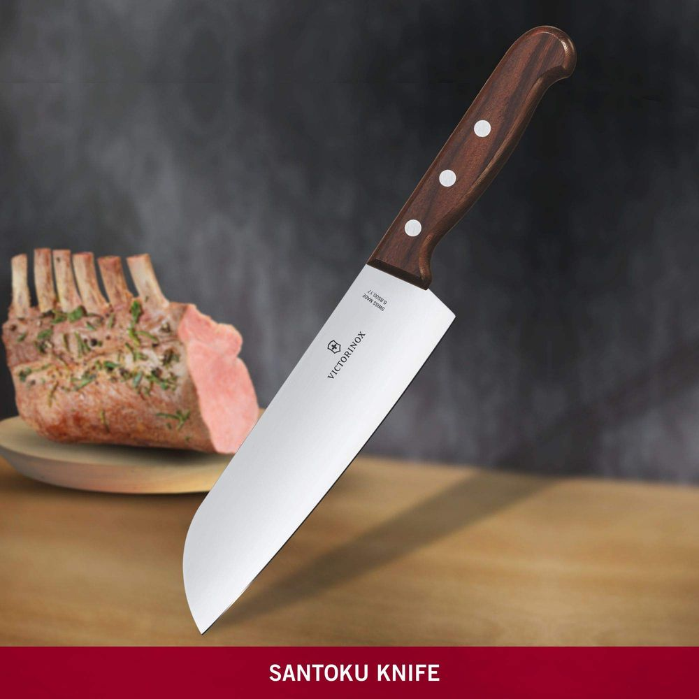 Ein Kochmesser mit Holzgriff neben einem rohen Rippchenbraten auf einem Holzteller.