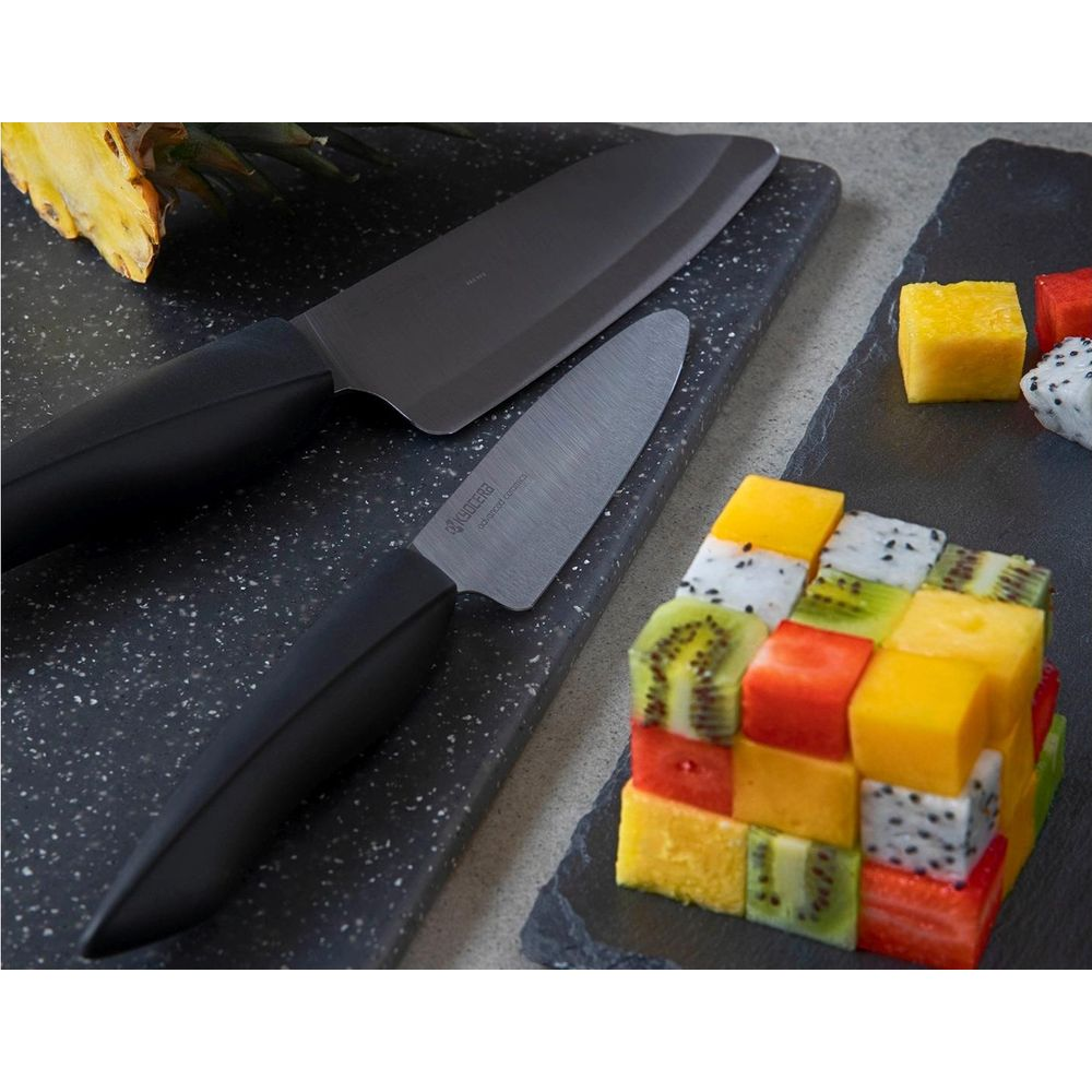 Deux couteaux reposent sur une planche à découper à côté d'un cube de fruits coupés.