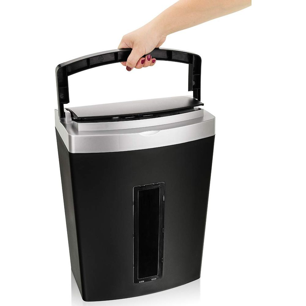 Ręka podnosi czarny niszczarka do papieru z srebrną ramką za uchwyt.