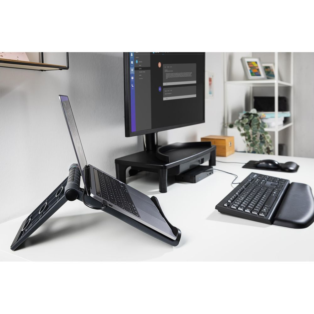 Un laptop su un supporto, vicino a monitor, tastiera e mouse su una scrivania.