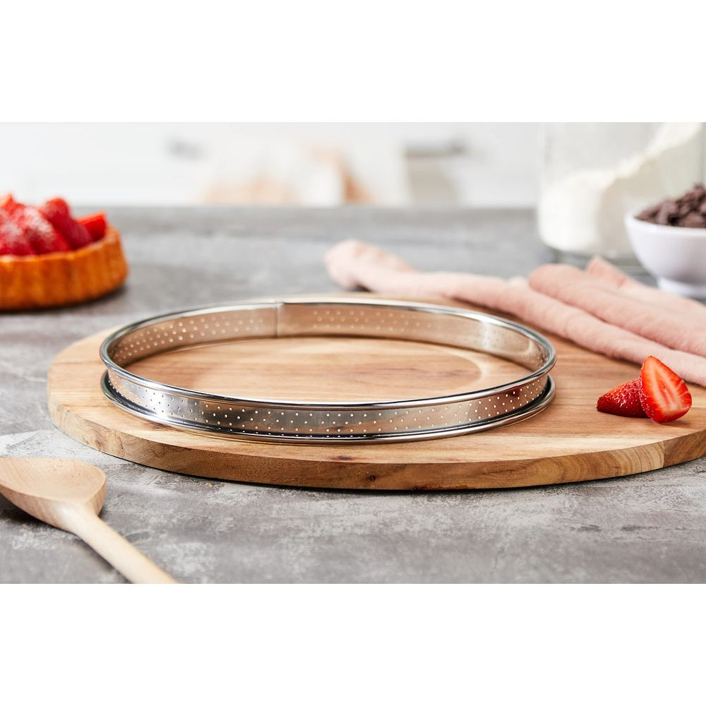 Un cercle à tarte perforé sur une planche en bois avec des fraises et des ustensiles.