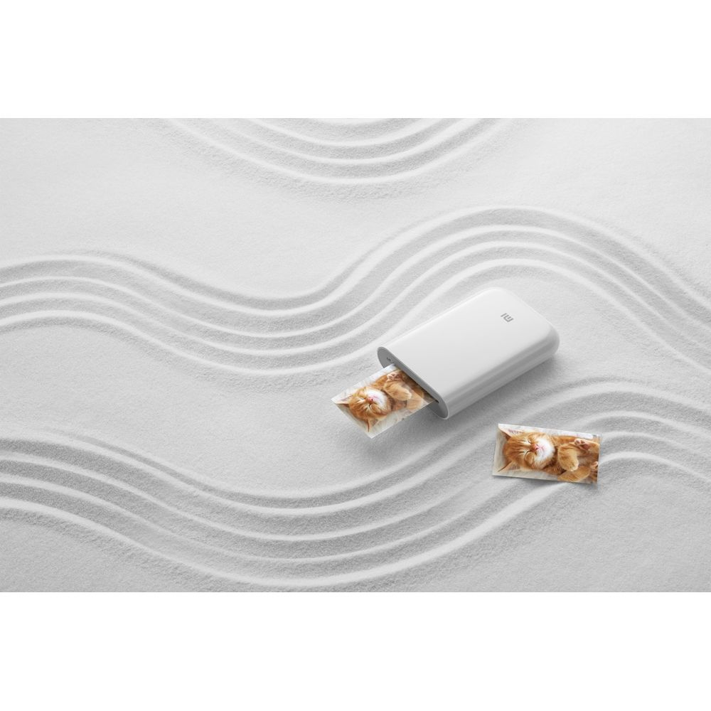 Biała drukarka drukuje zdjęcie kota na białym piasku.