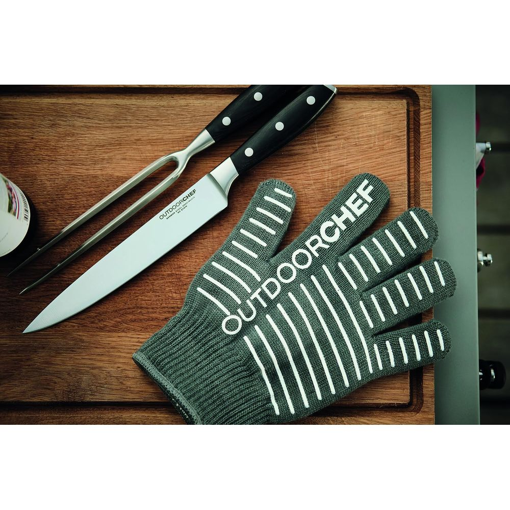 Rękawica grillowa, nóż i widelec do mięsa na desce.