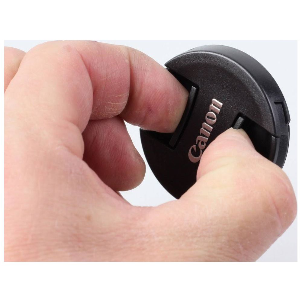 Dłoń naciska na czarny dekielek obiektywu Canon.