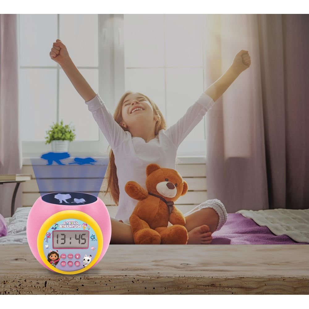 Una bambina si stiracchia accanto a un orsacchiotto e una sveglia con proiezione.