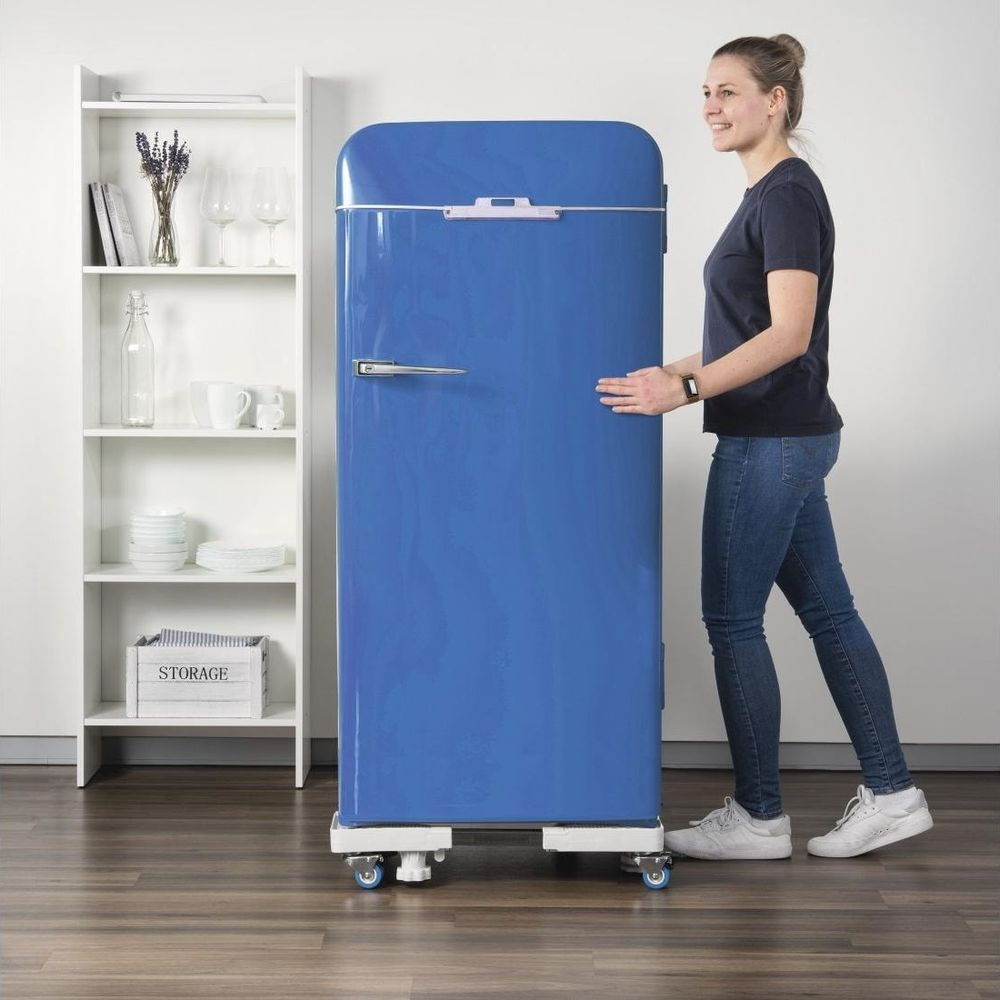 A woman pushes a blue refrigerator on wheels next to a shelf.