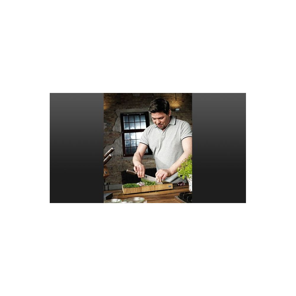 Mężczyzna w szarym polo sieka zioła na drewnianej desce.