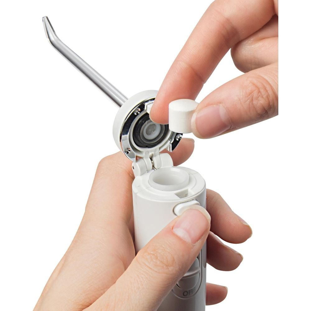 Mani inseriscono una compressa bianca in un dispositivo bianco con ugello metallico.