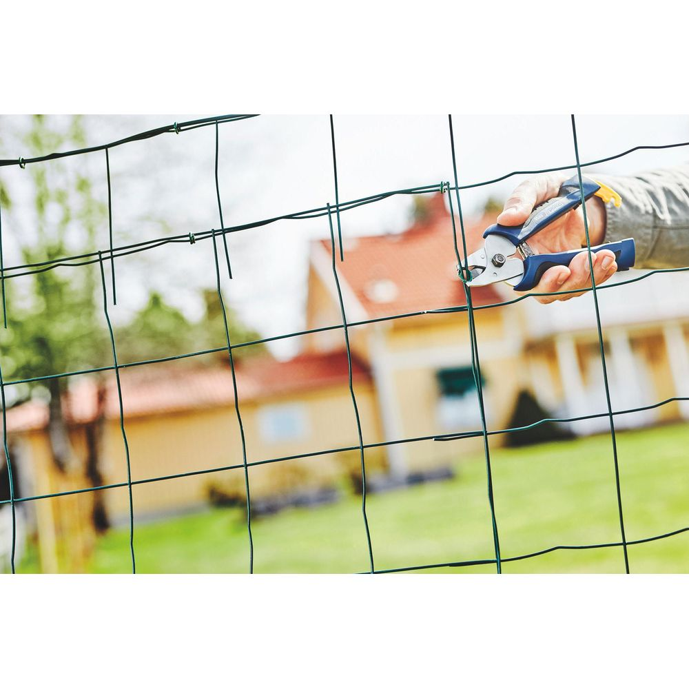 Hand with blue tool cutting wire fence in front of a house.