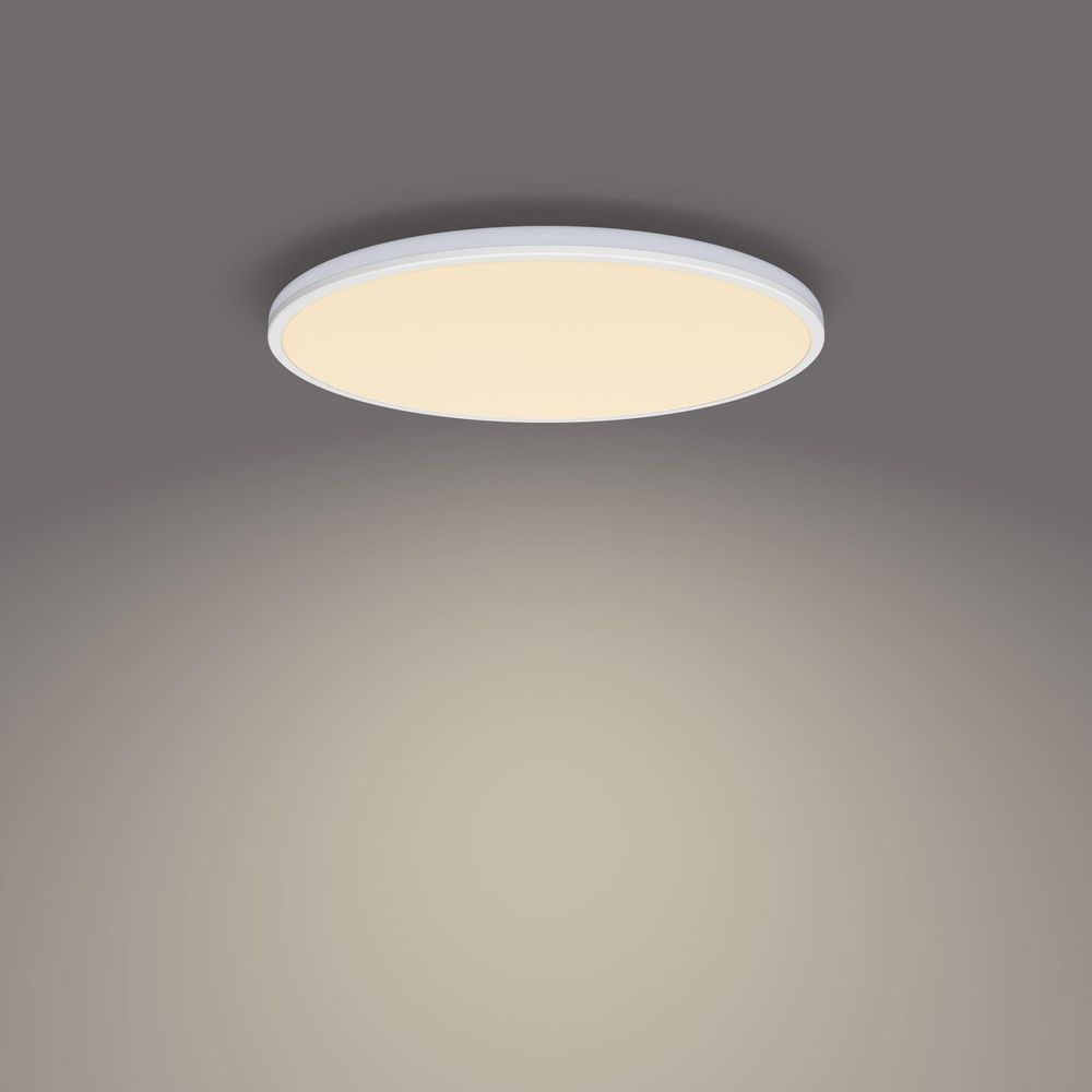 Un plafonnier rond et blanc émet une lumière chaude sur fond gris.