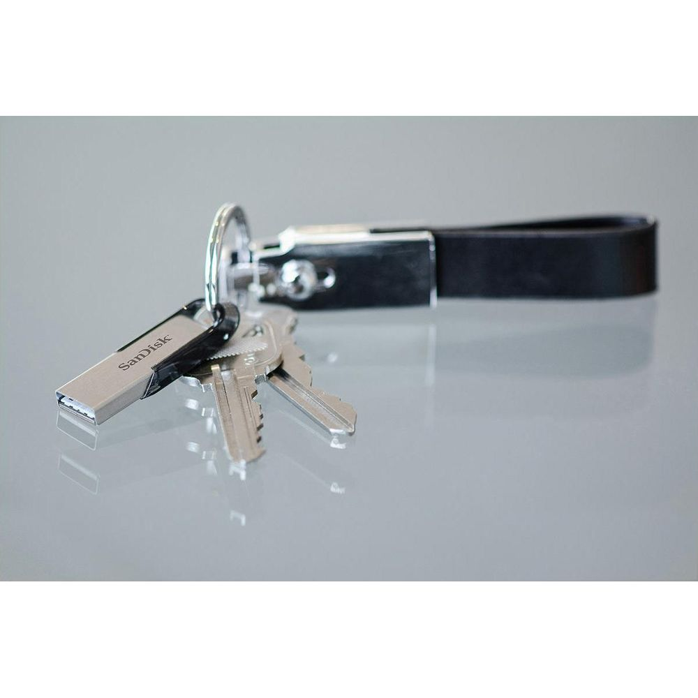 Una memoria USB y llaves en una correa de cuero negra sobre una superficie gris.