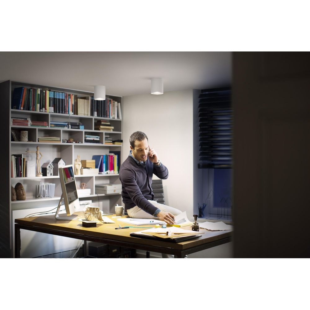 Mężczyzna siedzi na biurku i rozmawia przez telefon. Regał z książkami w tle.