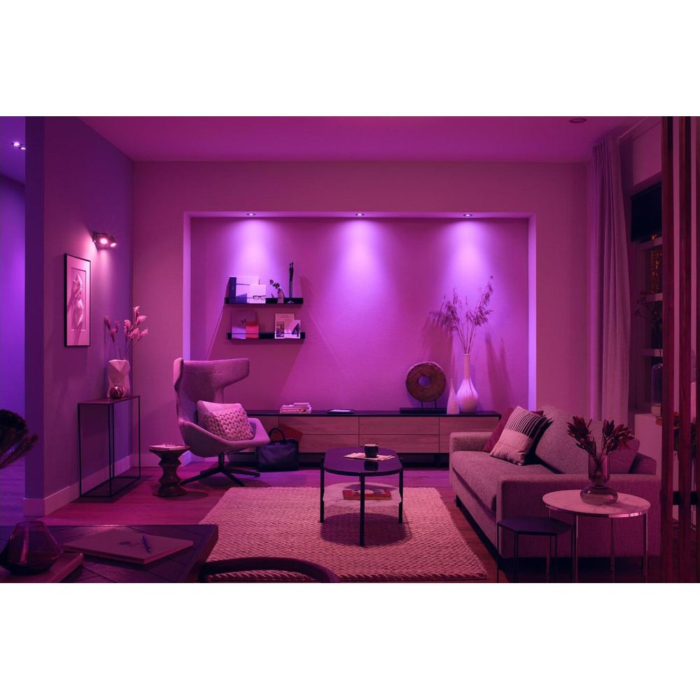 Een woonkamer met paarse verlichting, bank, fauteuil, salontafel en vloerkleed.