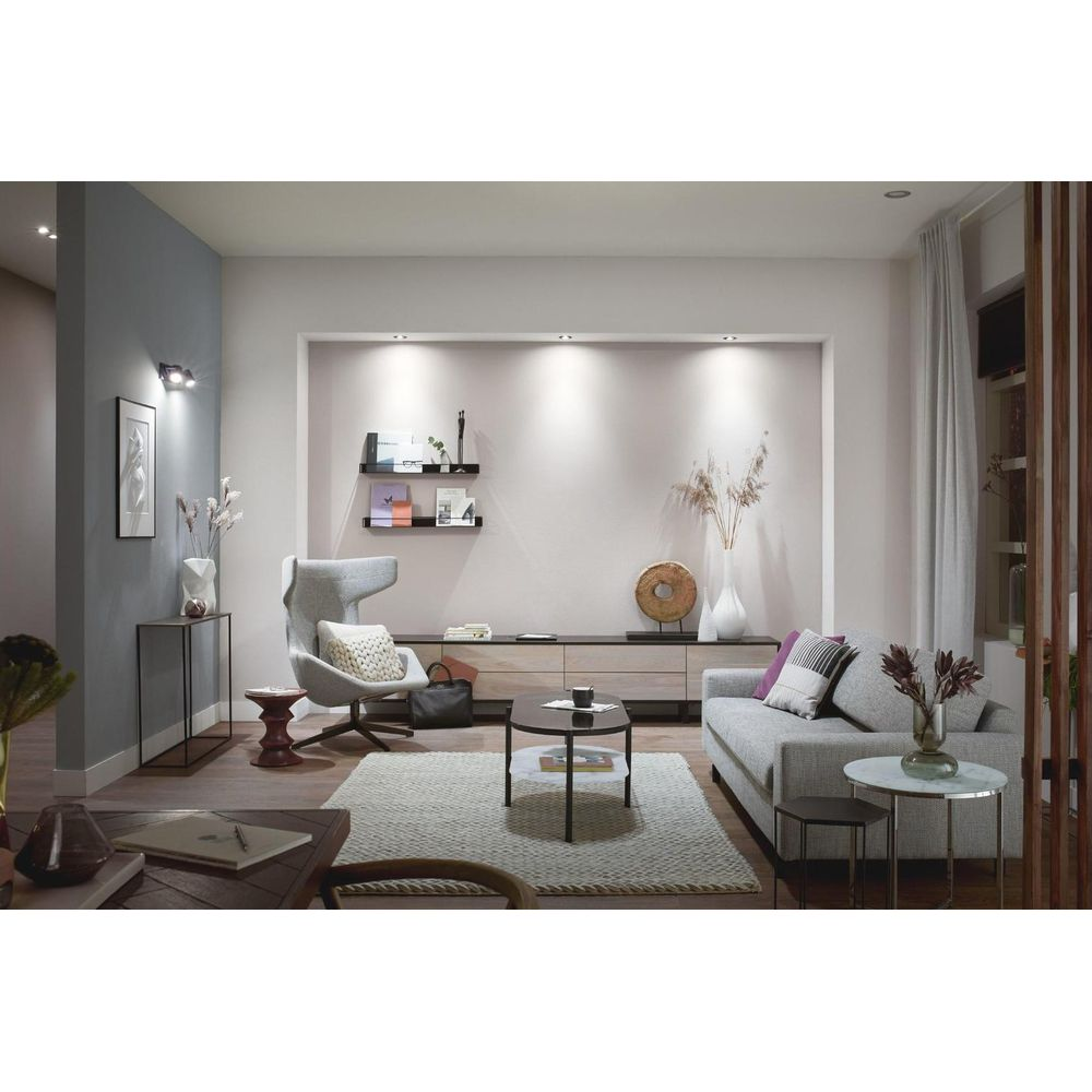 Moderne woonkamer met grijze bank, fauteuil, salontafels en wandplanken.