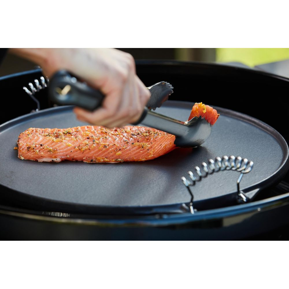 Ein Lachsfilet wird mit einer Zange auf einer Grillplatte platziert.