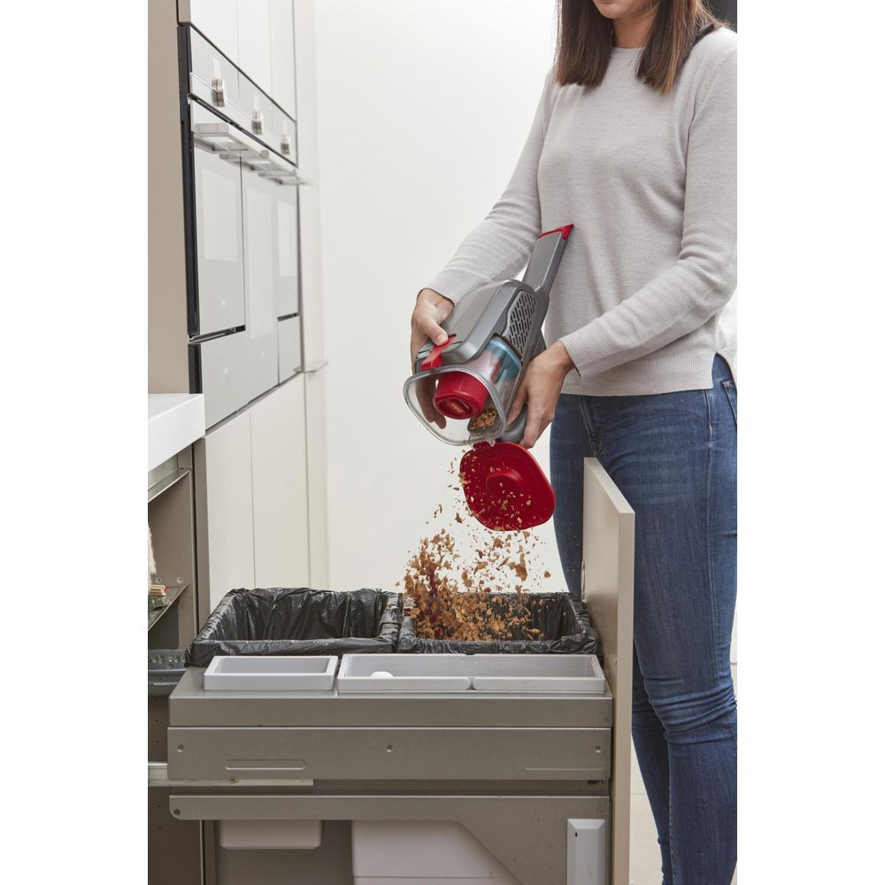 Una persona svuota un aspirapolvere portatile nei bidoni della spazzatura in cucina.
