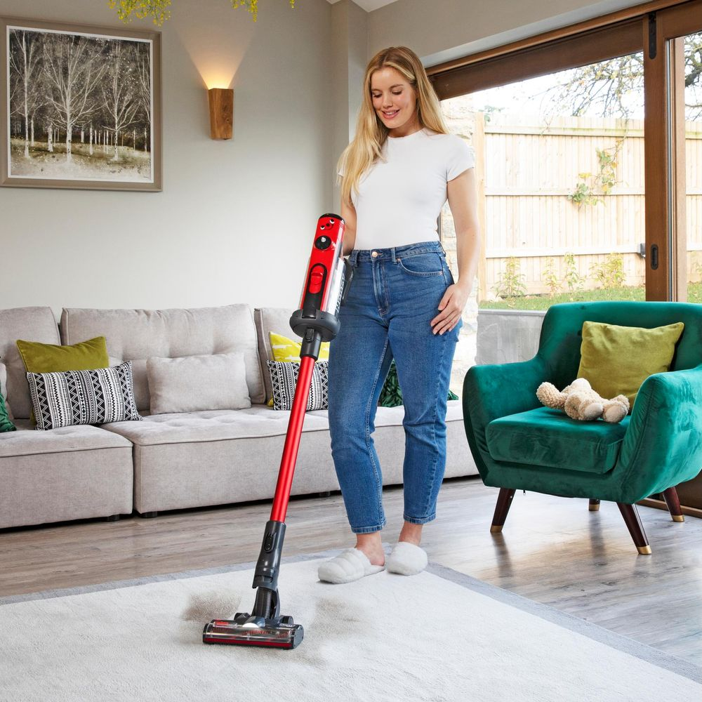 Een vrouw stofzuigt een tapijt in een woonkamer met een rode stofzuiger.