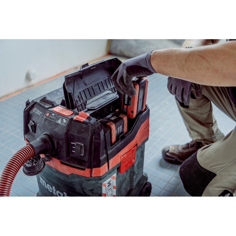 Persona inserisce batteria in aspirapolvere industriale rosso e nero.