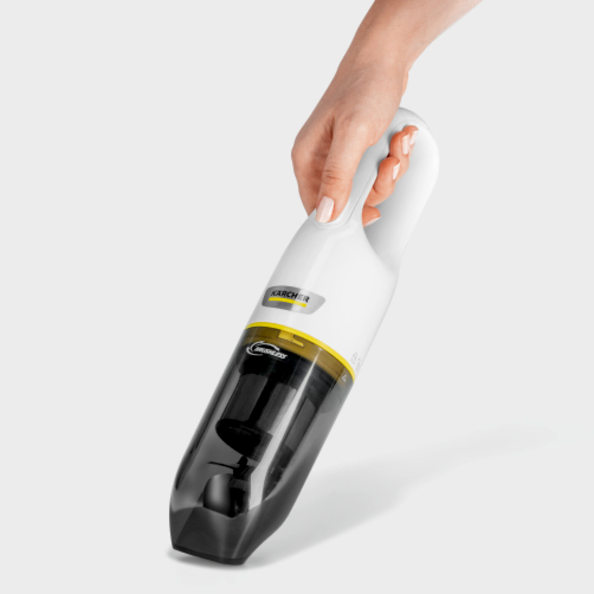 Une main tient un aspirateur à main Kärcher blanc avec un bac transparent.