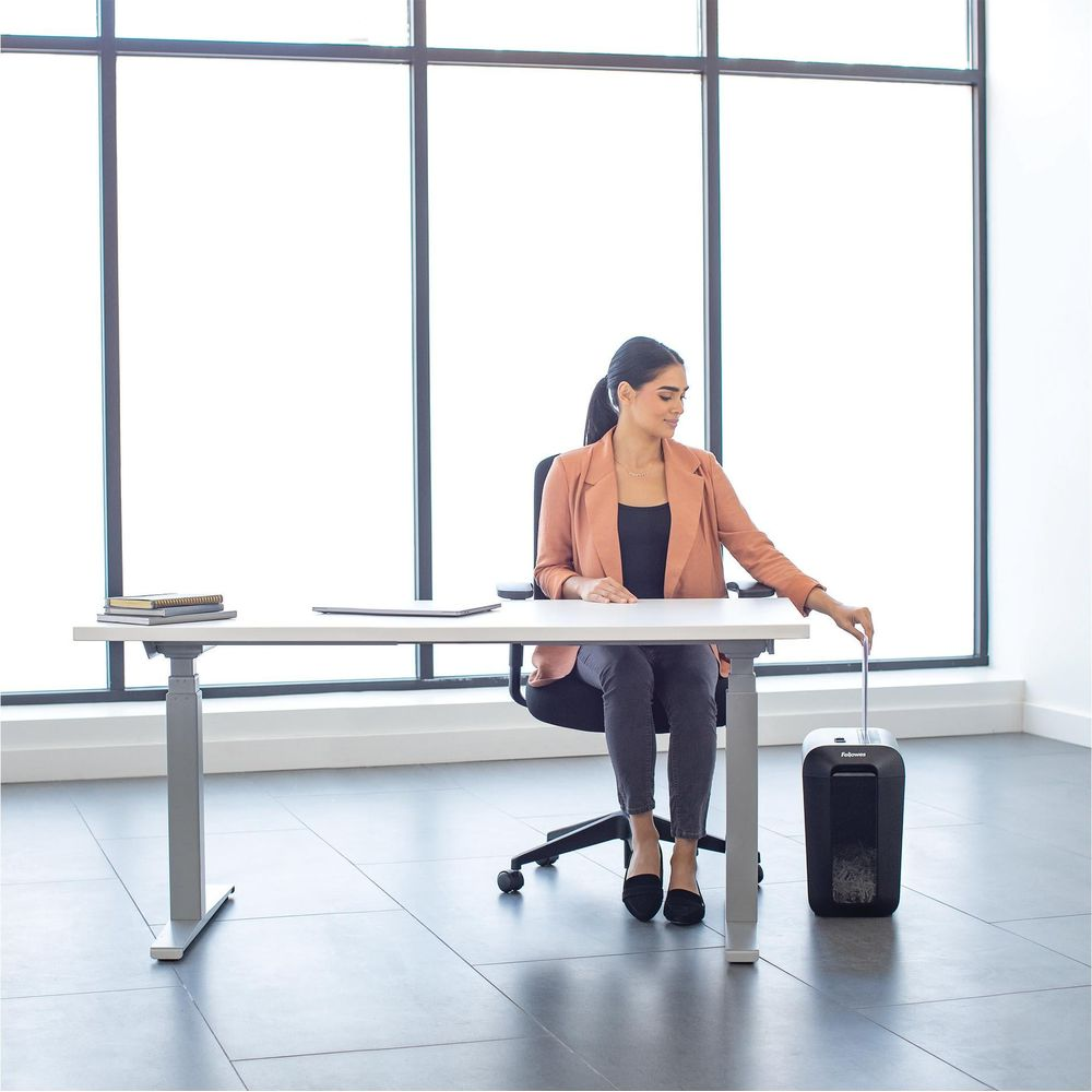 Femme à un bureau utilisant une déchiqueteuse, grandes fenêtres en arrière-plan.