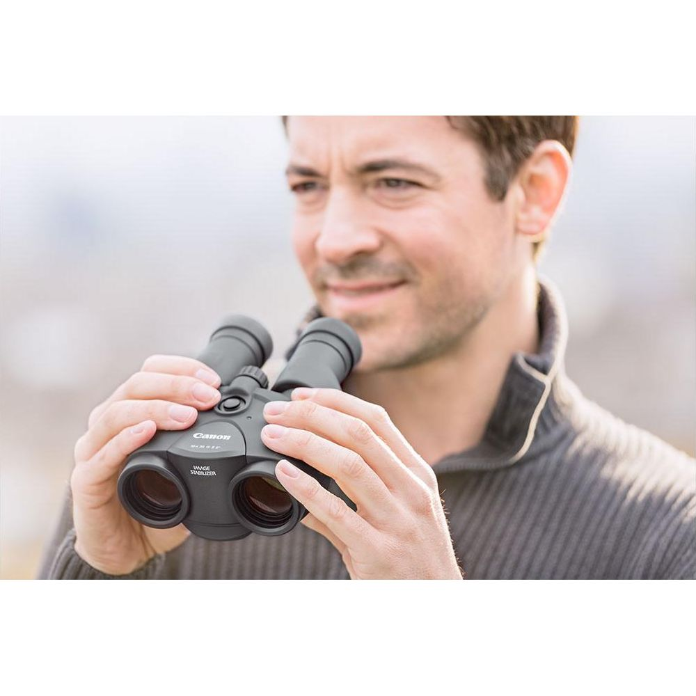 Mężczyzna trzyma lornetkę Canon ze stabilizacją obrazu na zewnątrz.