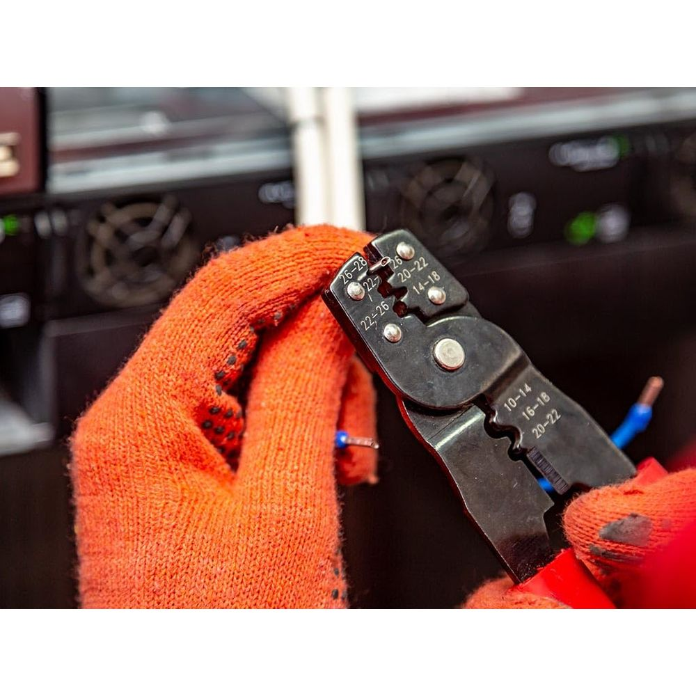 Dłonie w pomarańczowych rękawicach używają ściągacza izolacji do niebieskich przewodów.