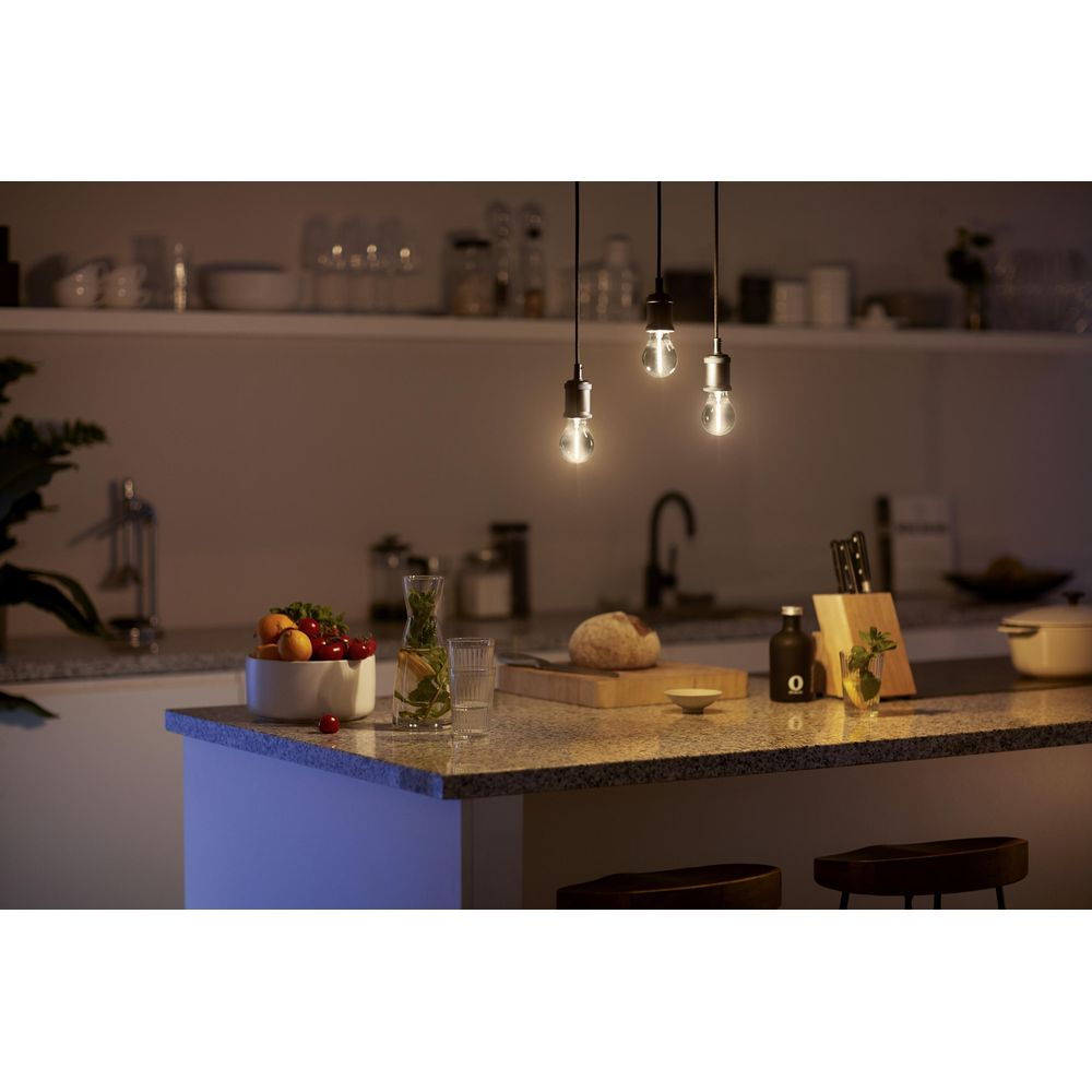 Trois ampoules pendent au-dessus d'un comptoir de cuisine avec des fruits et du pain.