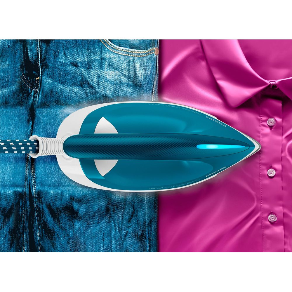 Un fer à vapeur bleu sur un jean et une chemise rose satinée.