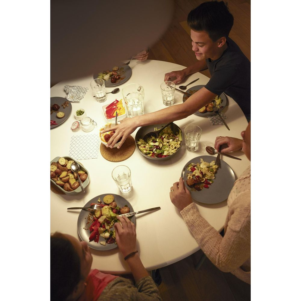 Des gens mangent un repas à une table ronde avec des assiettes, de la salade et des boissons.