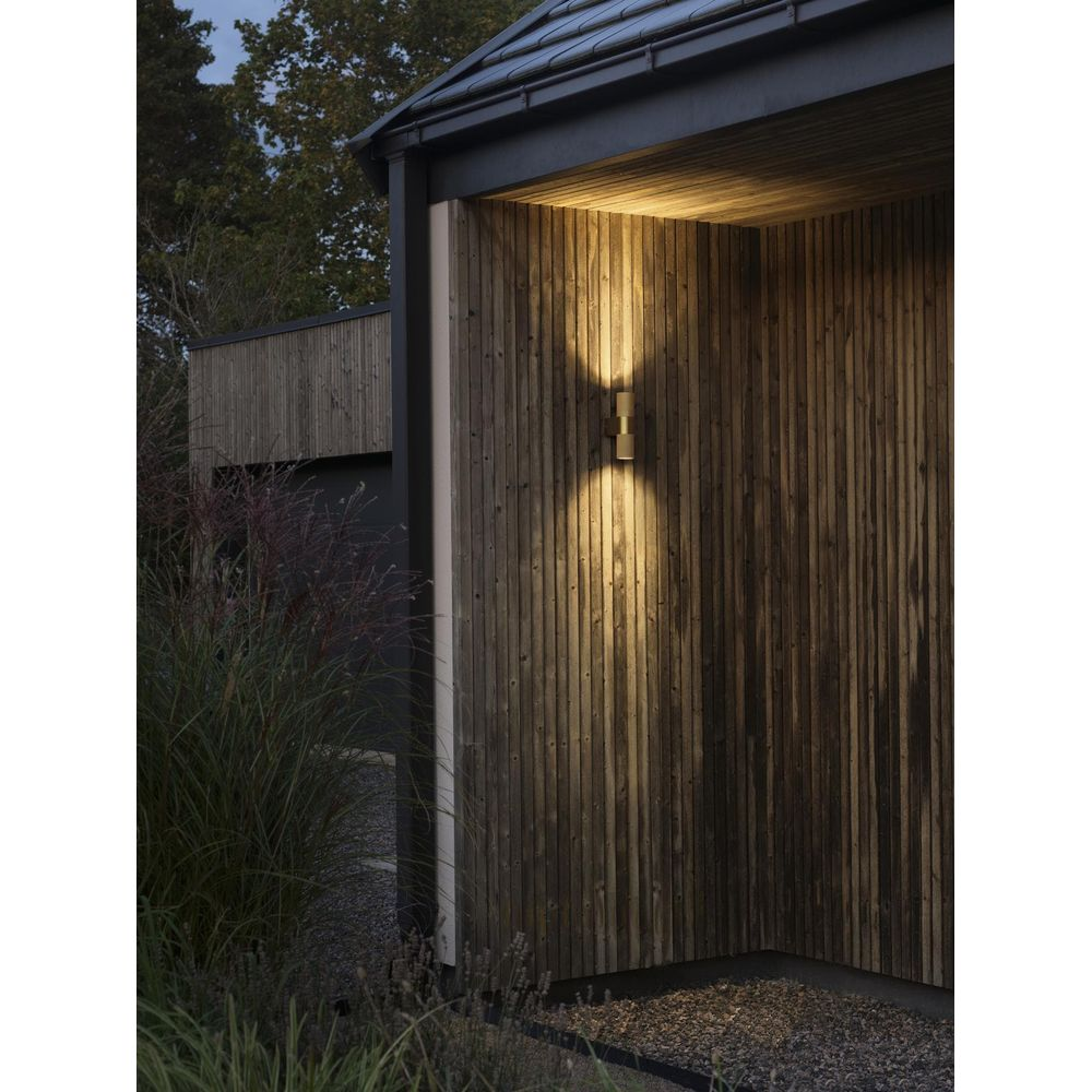 Ein moderner Außenwandleuchter beleuchtet eine Holzverkleidung bei Nacht.