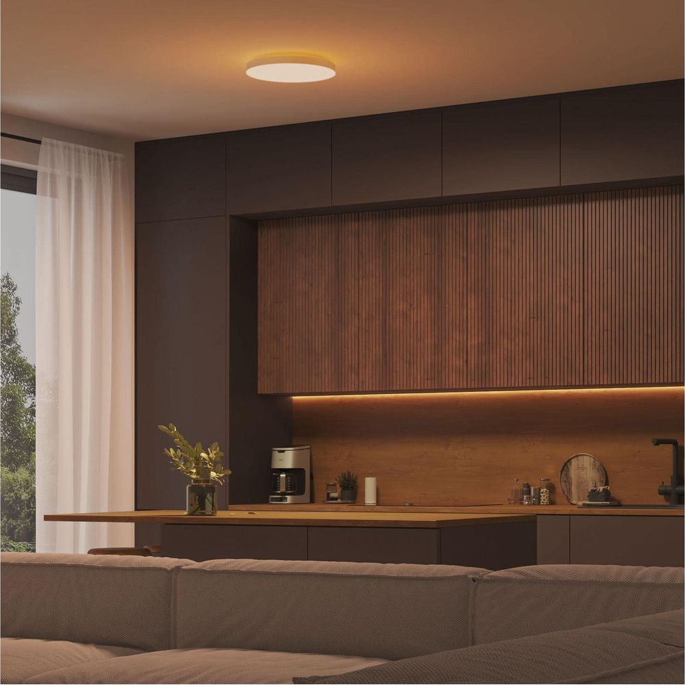 Nowoczesna kuchnia z ciemnymi drewnianymi szafkami, ekspresem i sofą.