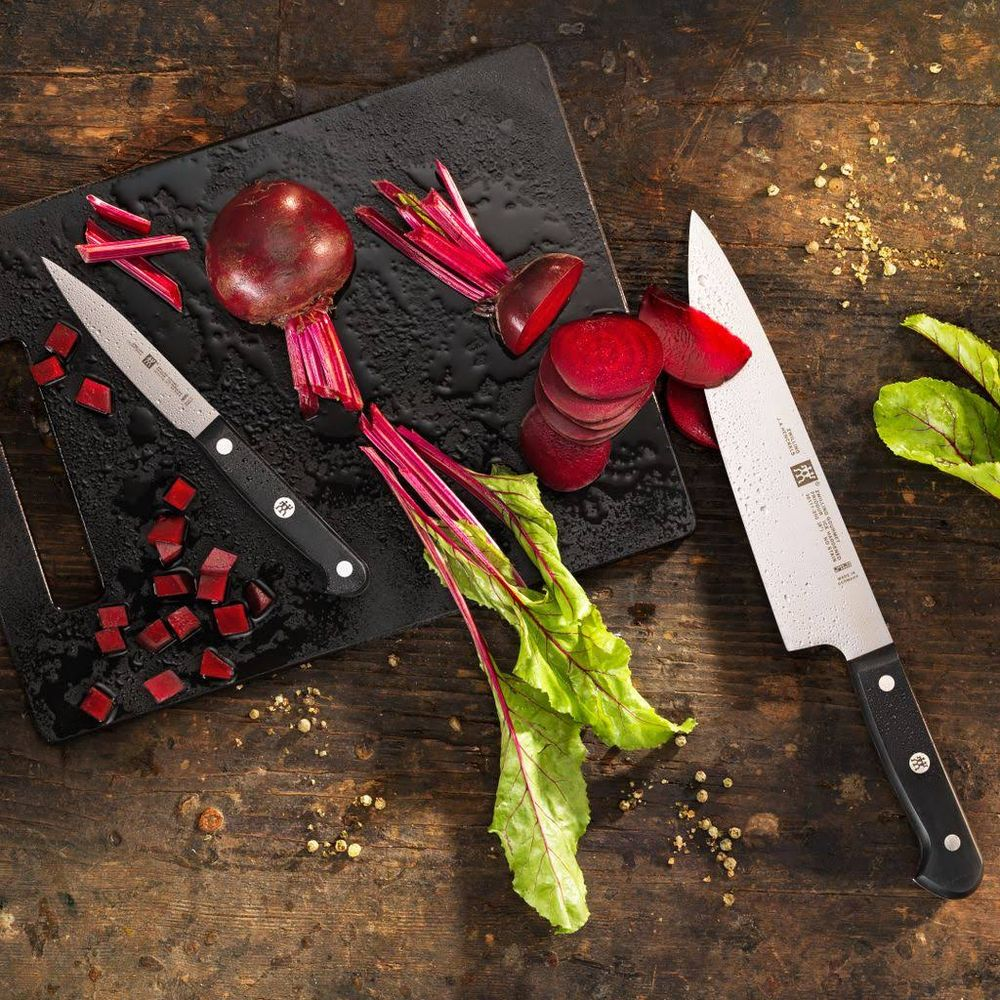 Buraki krojone na czarnej desce z nożami i liśćmi w pobliżu.