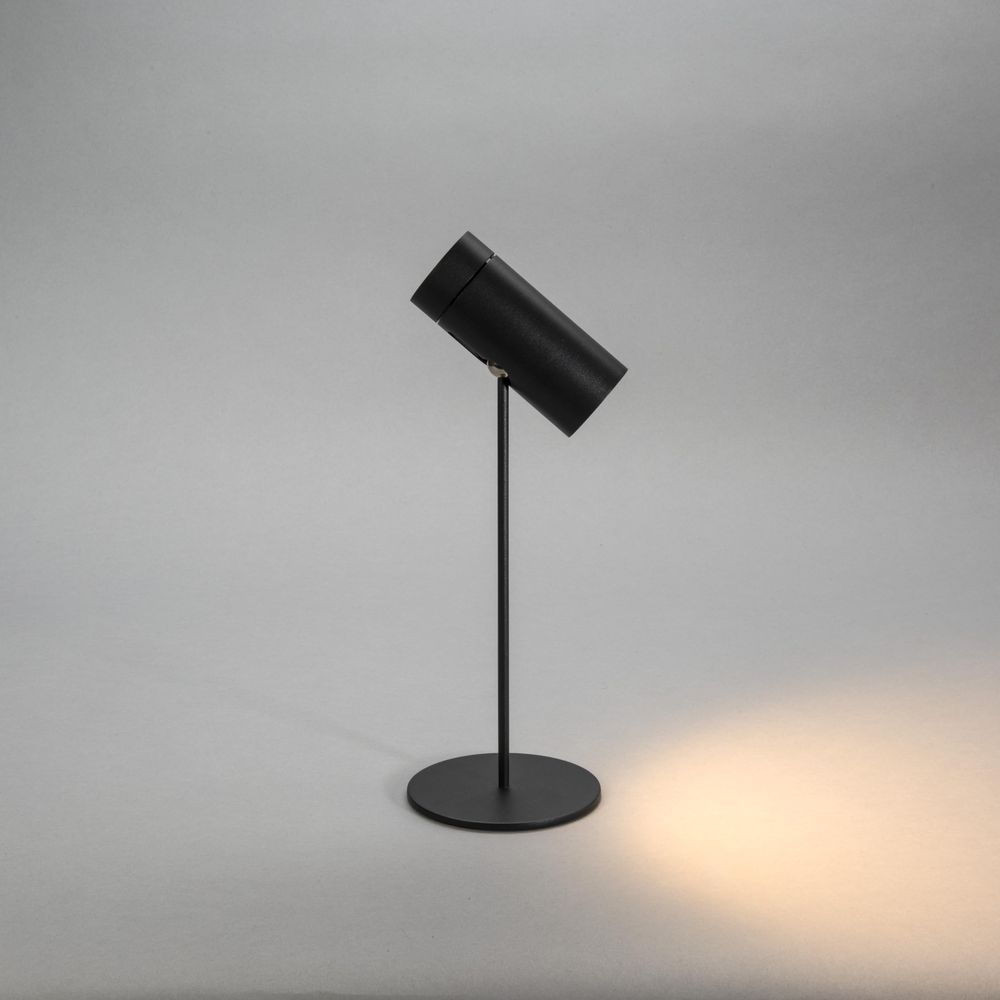Eine schwarze zylindrische Tischlampe mit einem schwenkbaren Kopf auf einem runden Sockel.