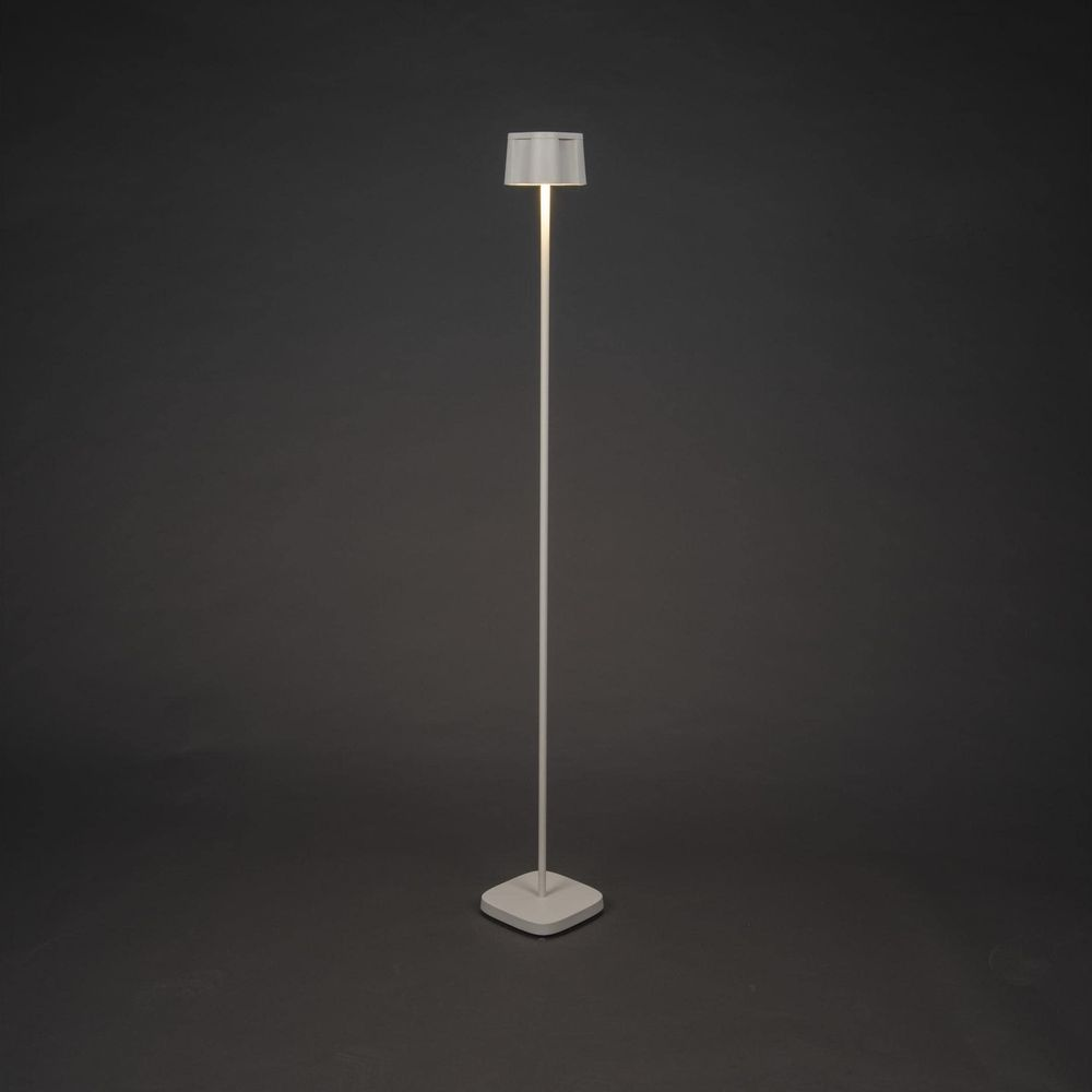 Eine schlanke, weiße Stehlampe mit einem zylindrischen Lampenschirm steht auf einem dunklen Hintergrund.