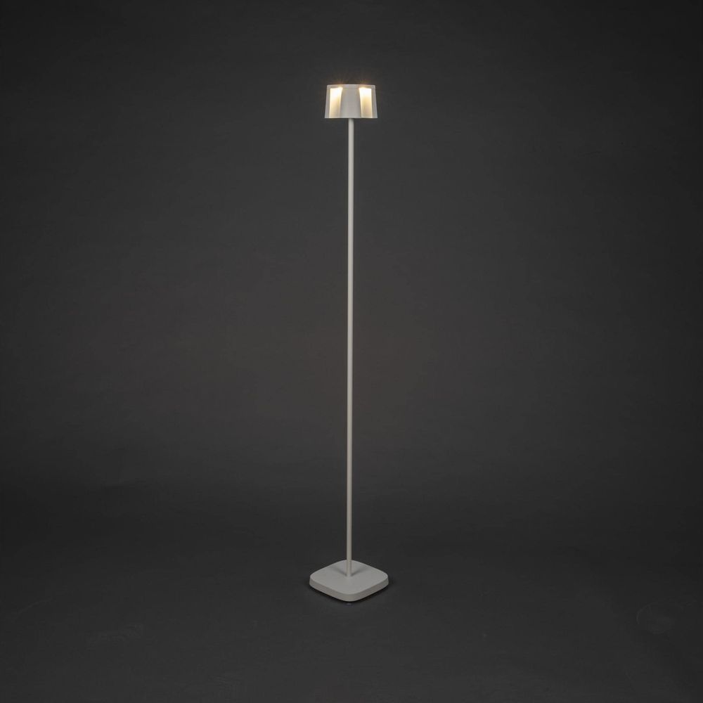 Eine weiße Stehlampe mit einem rechteckigen Lampenschirm leuchtet vor einem dunklen Hintergrund.