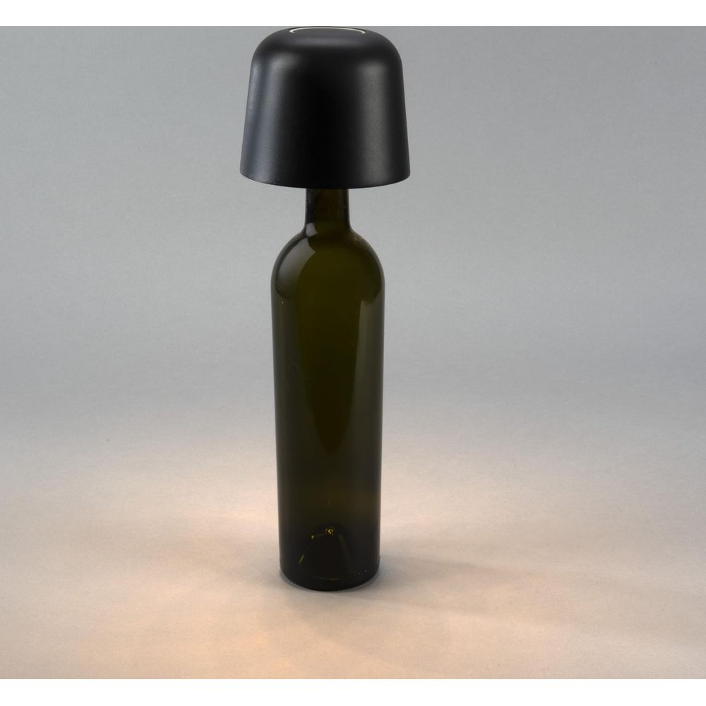 Eine grüne Glasflasche mit schwarzem Lampenschirm auf grauem Hintergrund.