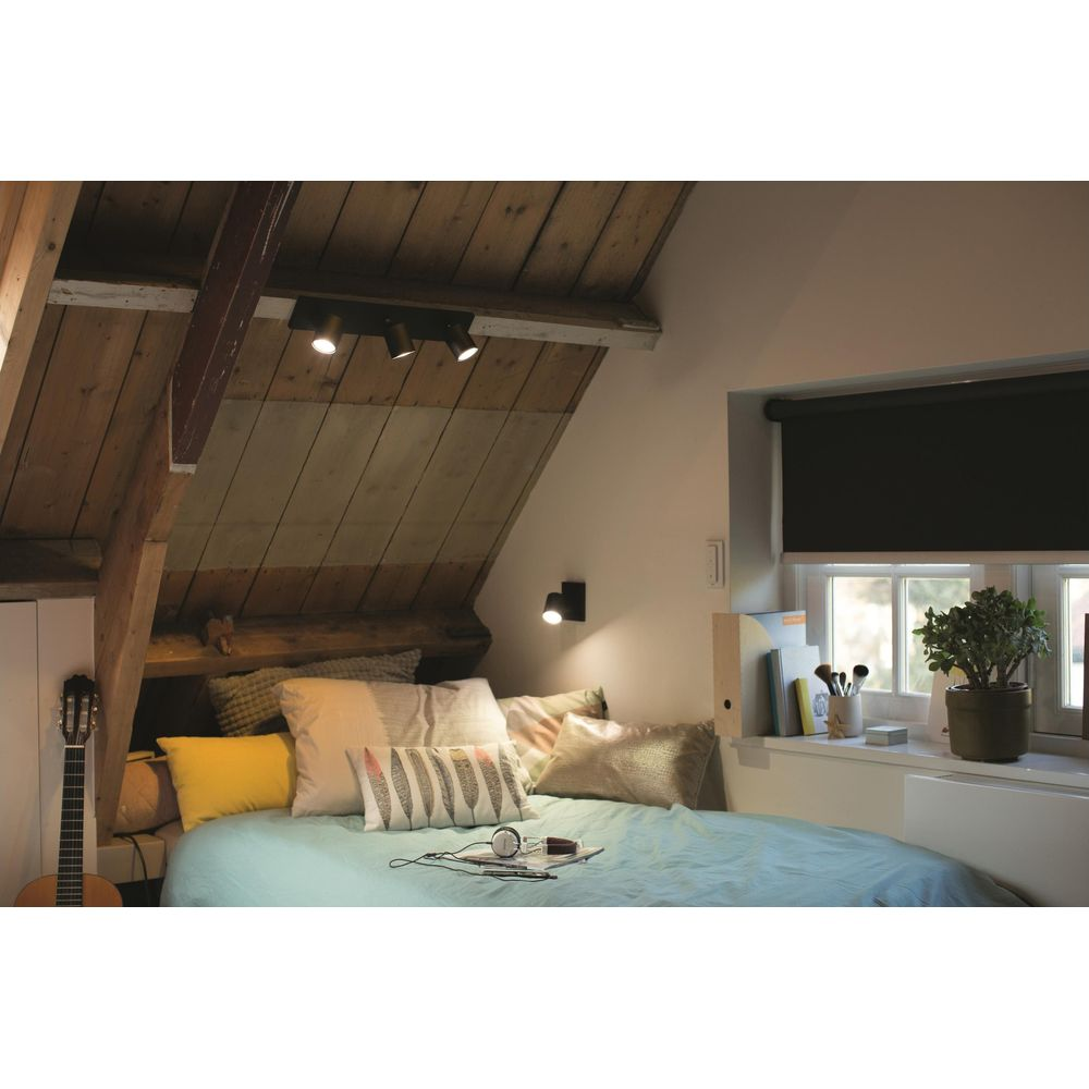Zolder slaapkamer met bed, gitaar, houten plafond en raam met planten.