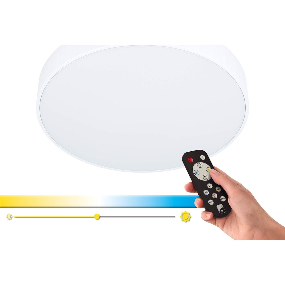 Une main tient une télécommande devant un plafonnier rond.