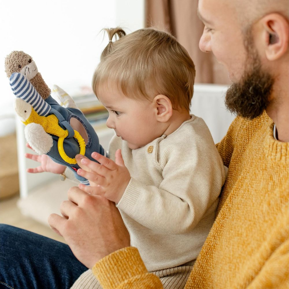 Un uomo con la barba gioca con un bambino che tiene un giocattolo morbido.