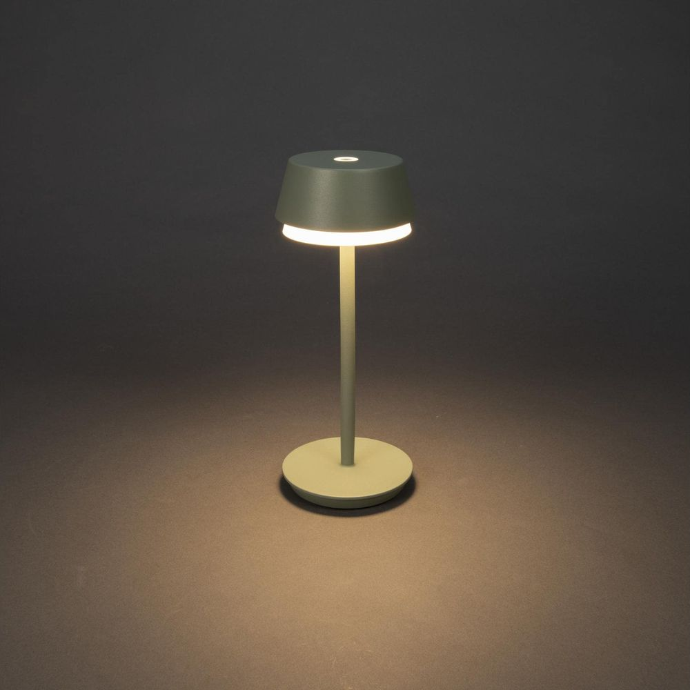 Eine grüne kabellose Lampe mit rundem Fuß und Schirm steht auf dunklem Grund.
