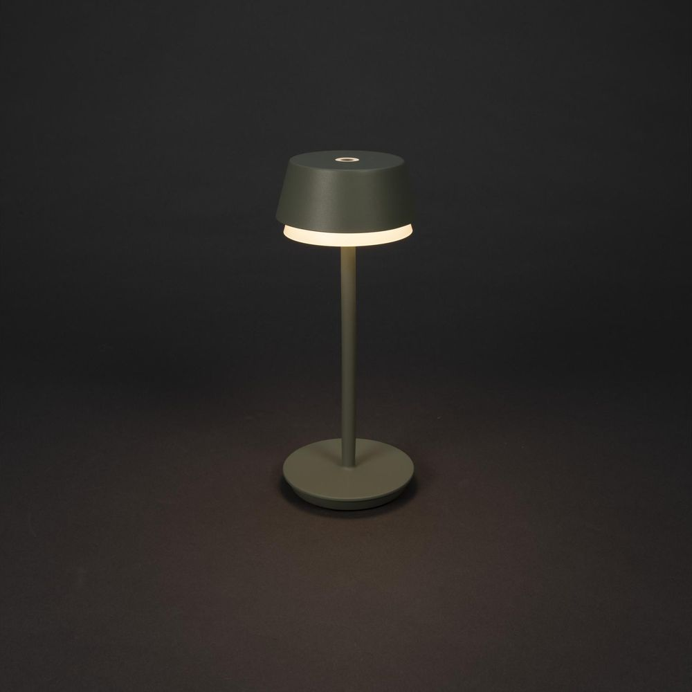 Eine grüne Lampe mit rundem Fuß und kegelförmigem Schirm leuchtet warm.
