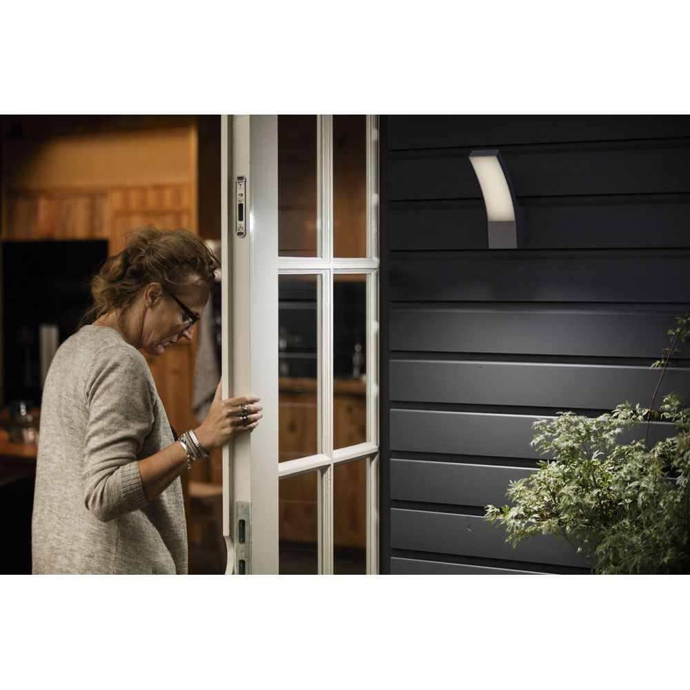 Eine Frau öffnet eine Tür zu einem Haus, draußen ist eine Wandlampe.
