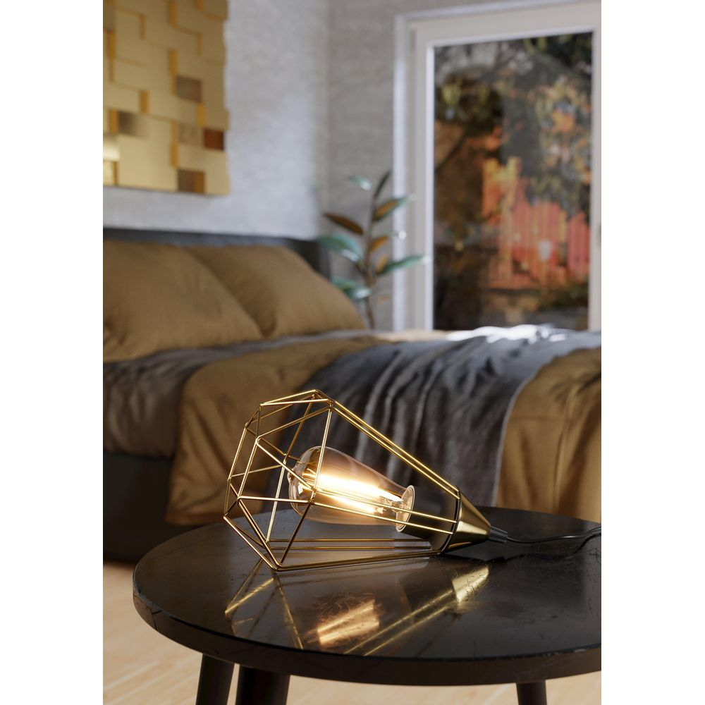 Abat-jour géométrique doré avec ampoule sur une table noire.