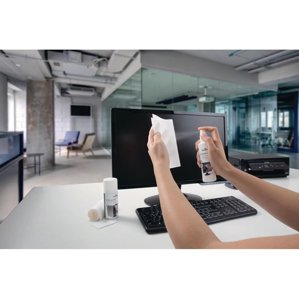 Persona pulisce monitor con spray e panno, tastiera e stampante vicine.