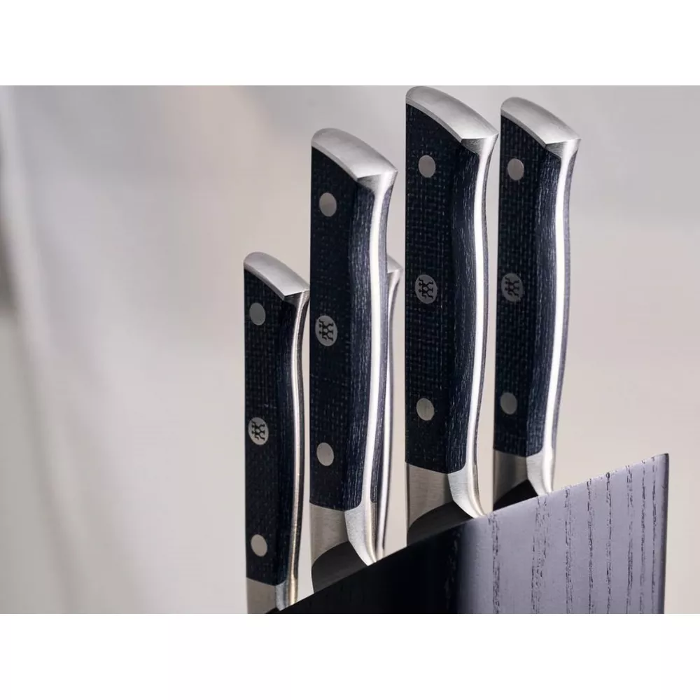 Cztery noże kuchenne z czarnymi rękojeściami i srebrnymi akcentami stoją w ciemnym drewnianym bloku.