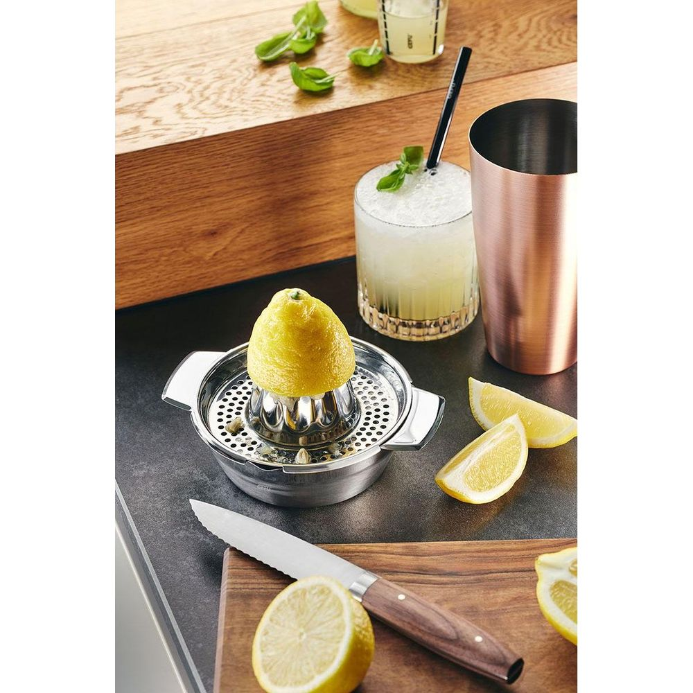 Eine Zitrone auf einem Entsafter neben einem Glas Cocktail und Zitronenspalten.