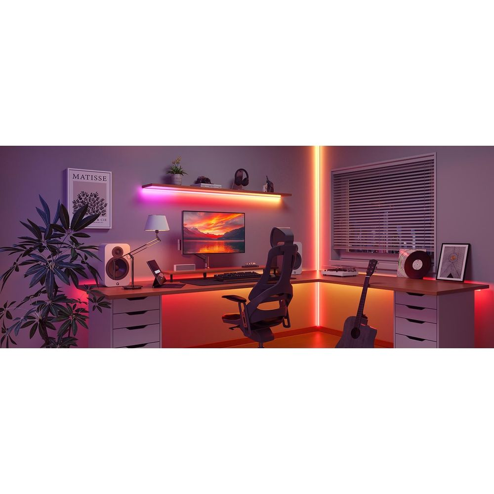 Una scrivania con monitor, sedia, altoparlanti, chitarra e piante, illuminata da luci LED colorate.