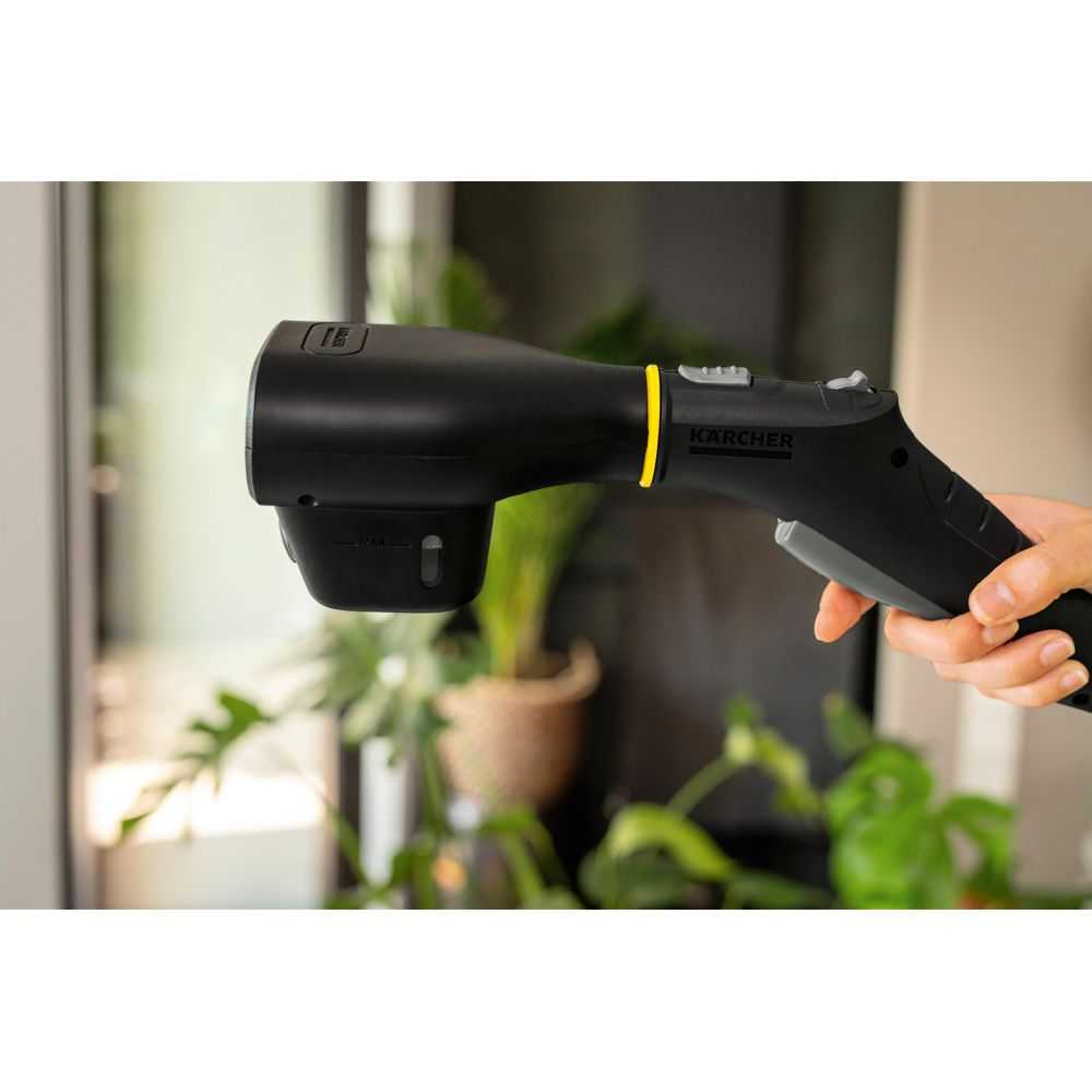 Schwarzer Kärcher Dampfreiniger in der Hand. Grüne Pflanzen im Hintergrund.